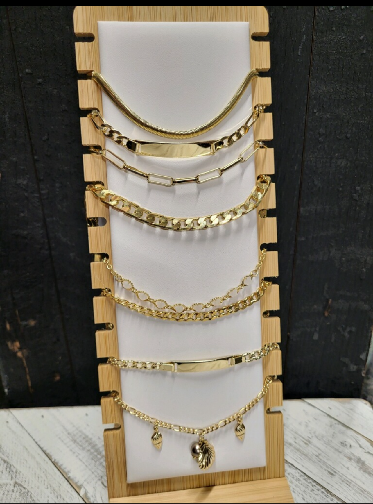 Eight gold bracelets on a bracelet holder. One of the bracelets have gold charms