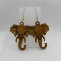 A pair of wooden elephant dangle earrings with rose gold fishhook wires, displayed on a clear plastic stand against a white textured background.